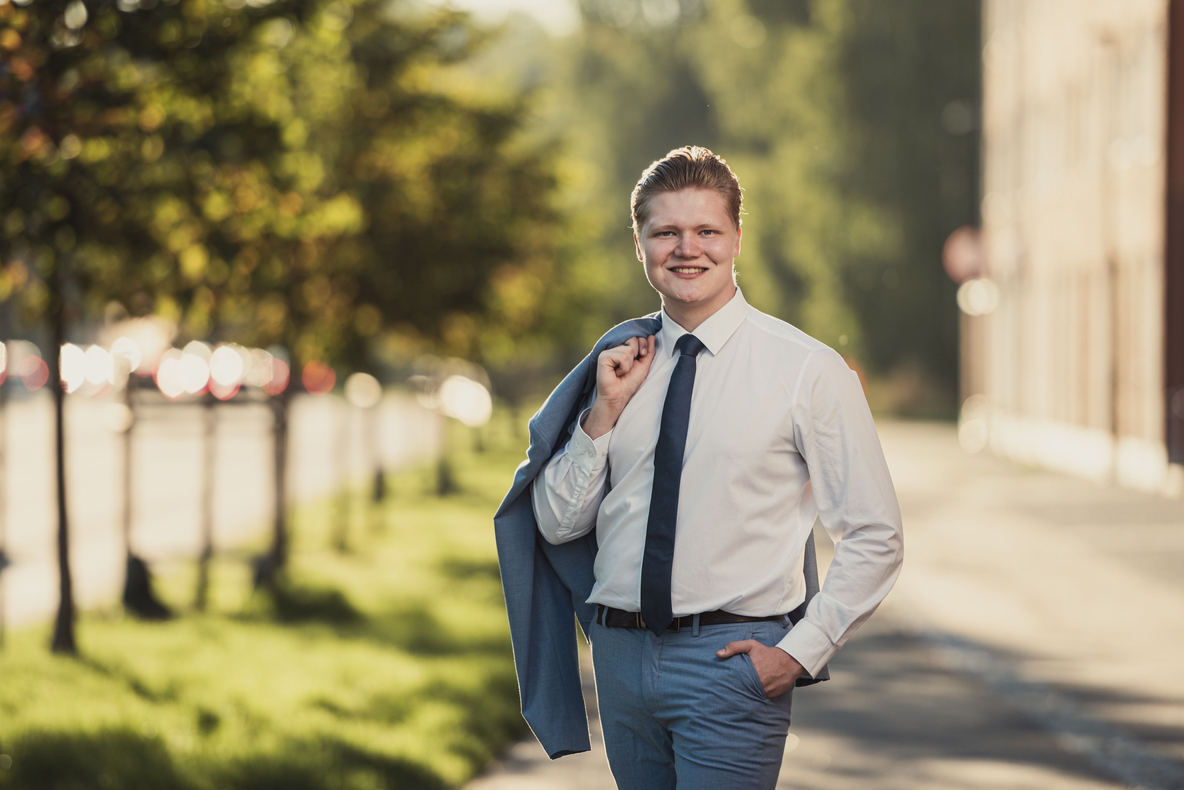 Martti Paldanius, nuori kokoomusnuori hymyilee aurinkoisessa puistomaisemassa, pukeutuneena valkoiseen kauluspaitaan ja siniseen solmioon, sininen puvuntakki olalla